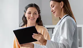 female doctor with tablet computer talking to smiling woman patient at hospital