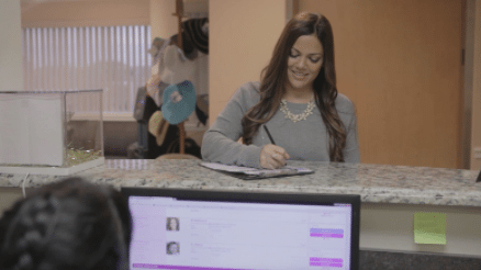 female patient at desk checking in while staff uses practice management software on computer