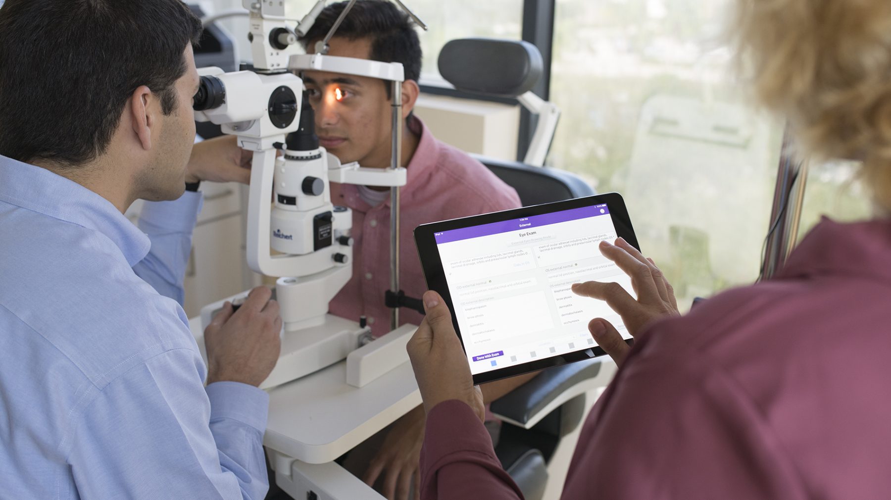 ophthalmologist examining a patient and medical assistant using and ophthalmology EMR
