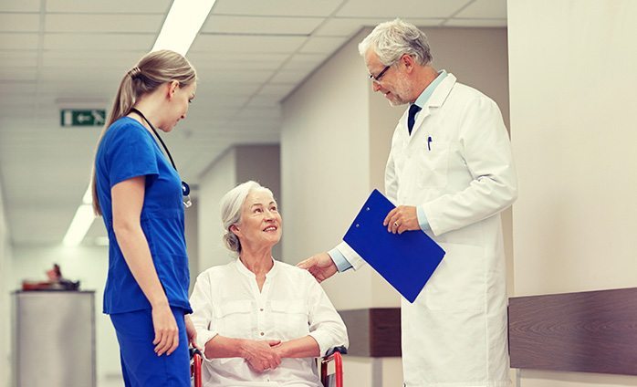 doctor and medical staff talking with elderly female patient in wheelchair