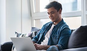 smiling male patient sitting on couch at home using laptop