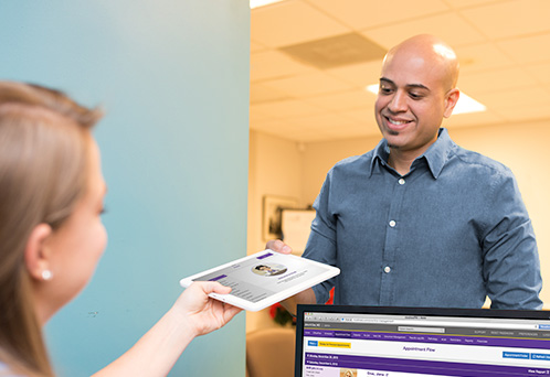 front desk staff handing smiling patient an iPad