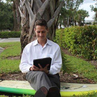 Dr. David Lehman sitting on a bench by a tree and using an iPad