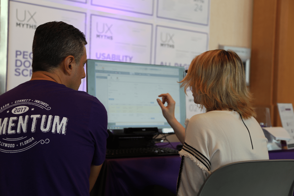 man in purple shirt looking at a computer screen with a woman pointing at the screen