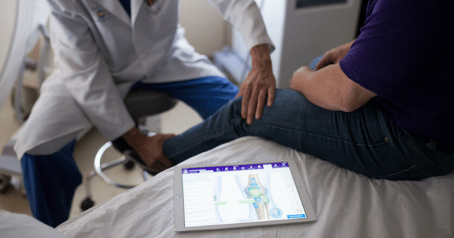 orthopedic-ehr-system orthopedic ehr ipad on exam table with doctor examining patient