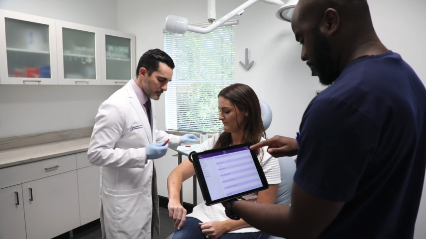 dermatologist examining a patient with medical assistant documenting on an iPad dermatology EHR