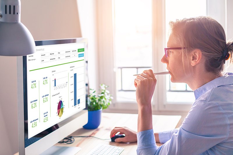 woman with pen in her mouth observing charts and graphs on desktop computer screen