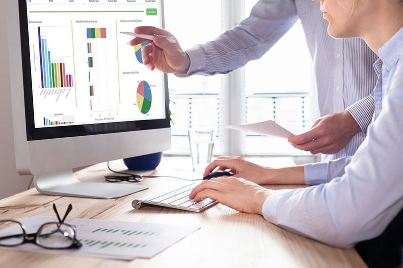 man pointing with a pen at a desktop screen with charts and graphs