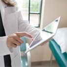 doctor in lab coat tapping EMA on an iPad in front of window doctor in lab coat tapping EMA on an iPad in front of window
