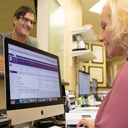 patient standing at counter while front desk staff uses practice management on desktop