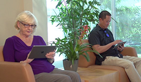 smiling male patient sitting on couch at home using laptop