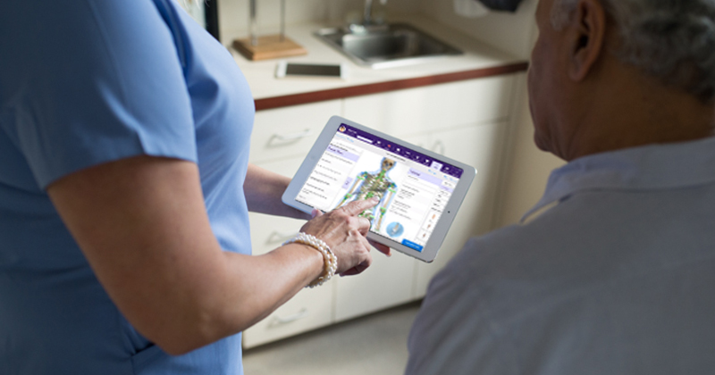 female medical assistant in blue scrubs pointing at orthopedic iPad EHR