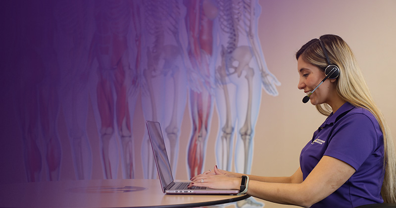 Woman wearing headset on laptop computer in front of medical wall mural