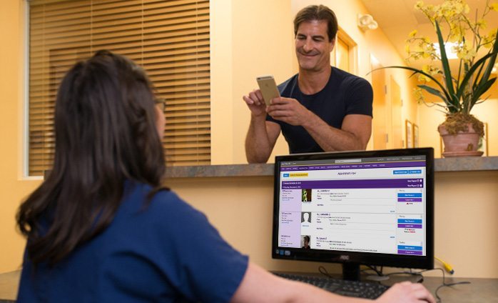 patient at front desk using patient portal on smartphone while staff uses practice management on desktop