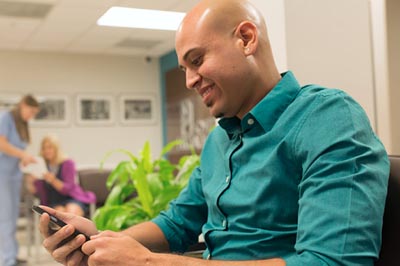 Patient sitting in waiting room uses his cell phone.