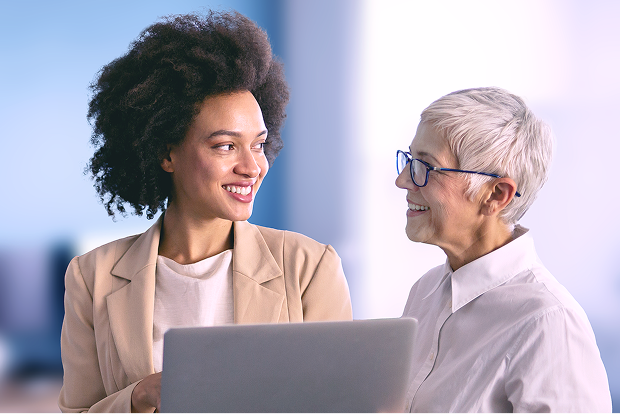Two professional women smiling and discussing something on a laptop in a modern office setting