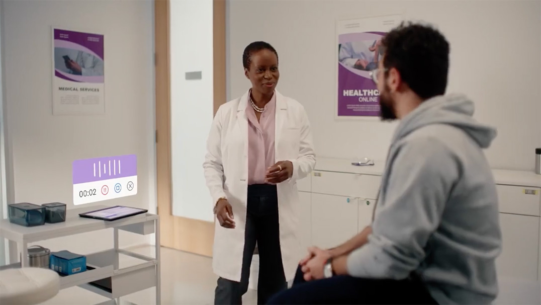 Doctor speaking with a patient in an exam room with a digital audio recording interface displayed near a tablet.