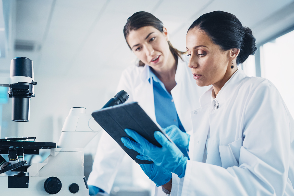 Two physicians in a laboratory setting collaborate over a tablet EHR, reviewing patient data next to a microscope.