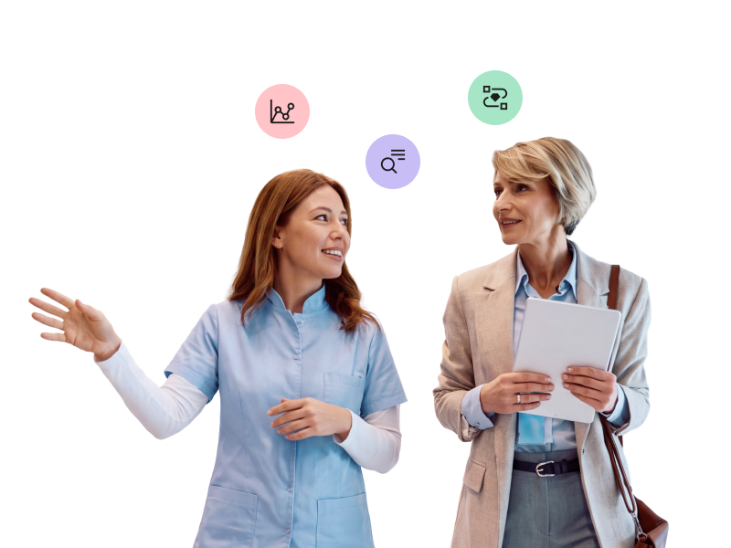 A healthcare worker in blue scrubs speaking and gesturing to a woman in professional business attire who is holding a tablet, with floating icons of a line graph, a magnifying glass, and a flowchart above them.