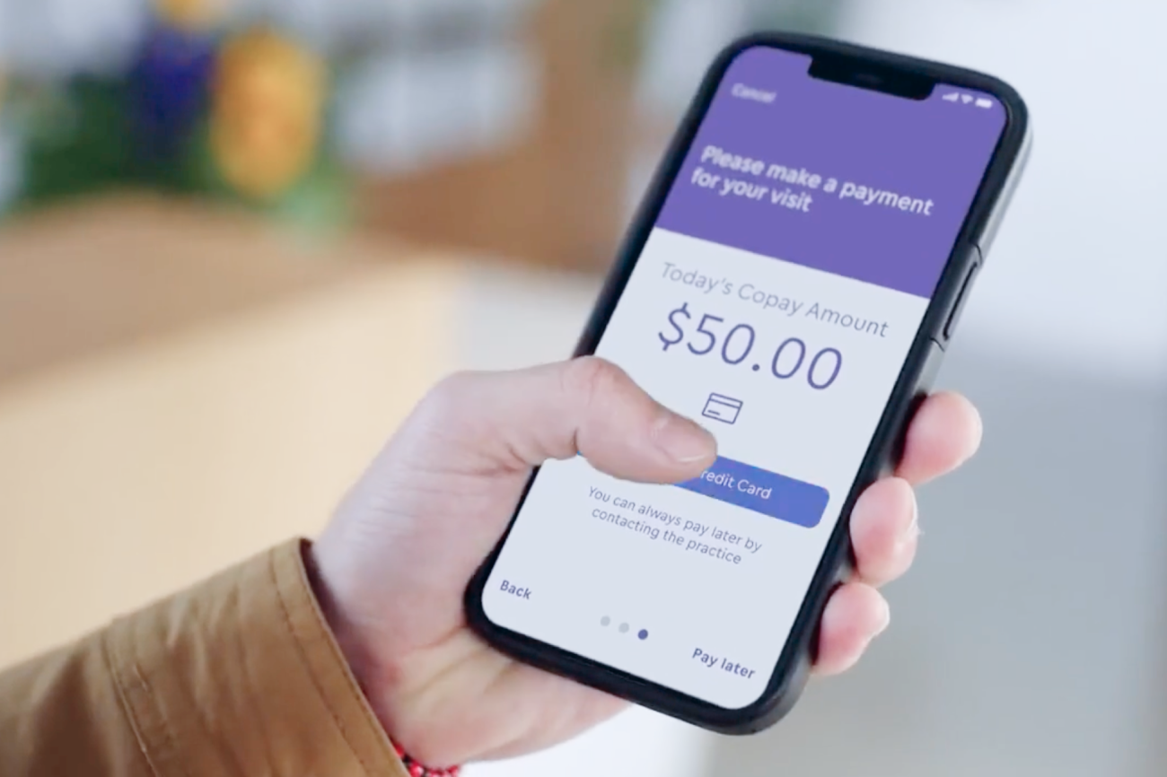 Una mano que sostiene un smartphone en el que se ve la pantalla de pago de un copago de 50,00 dólares por una visita.
