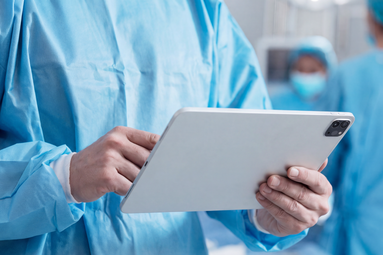 Un médico con una bata quirúrgica azul que sostiene una tableta en un quirófano.
