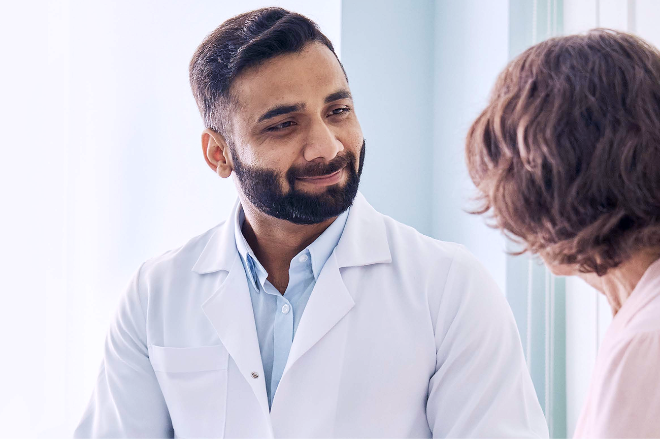 Médico sonriente con bata blanca hablando con un paciente durante una consulta.